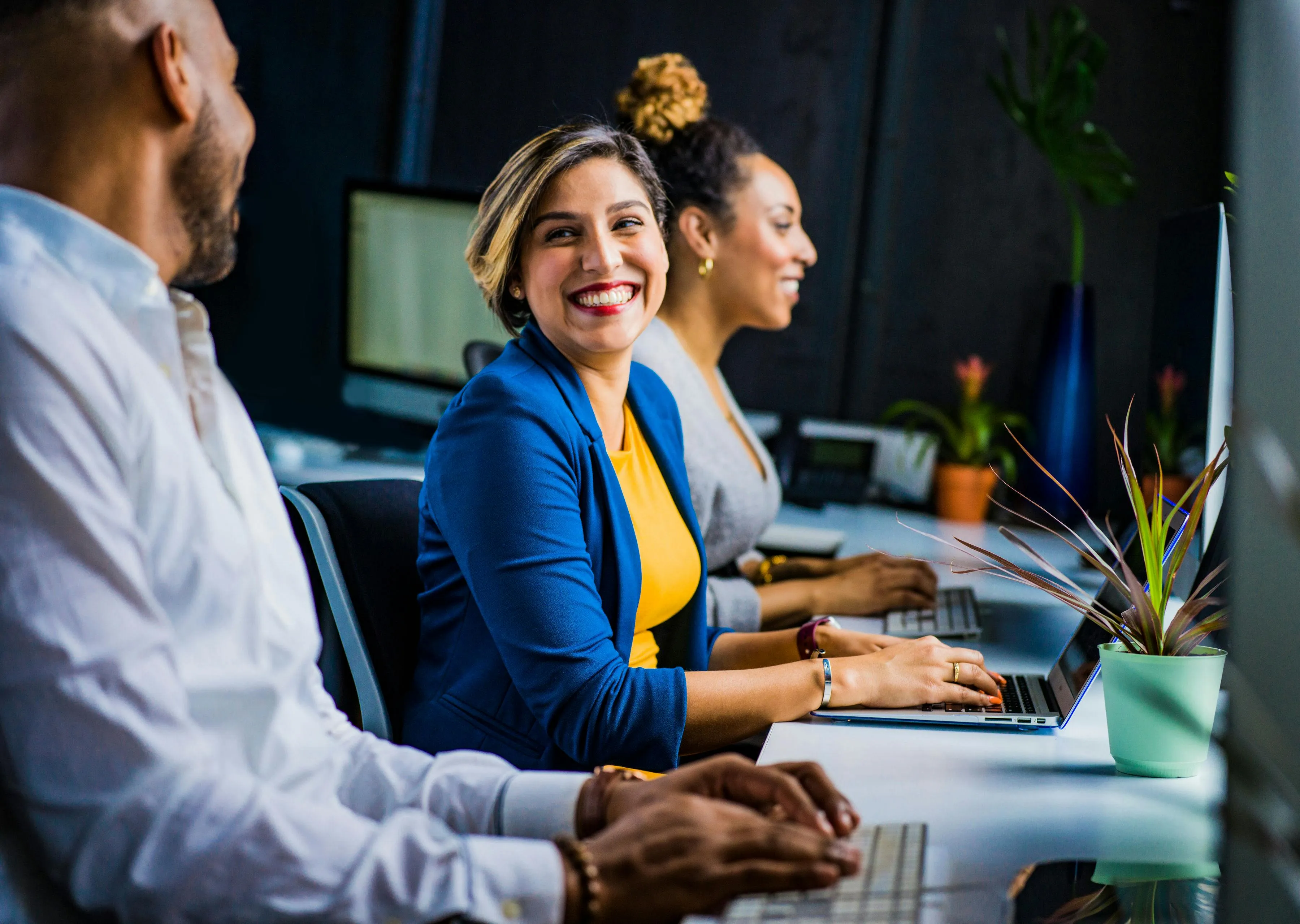 Colleagues working at their desks in an open-plan office, smiling during a conversation
