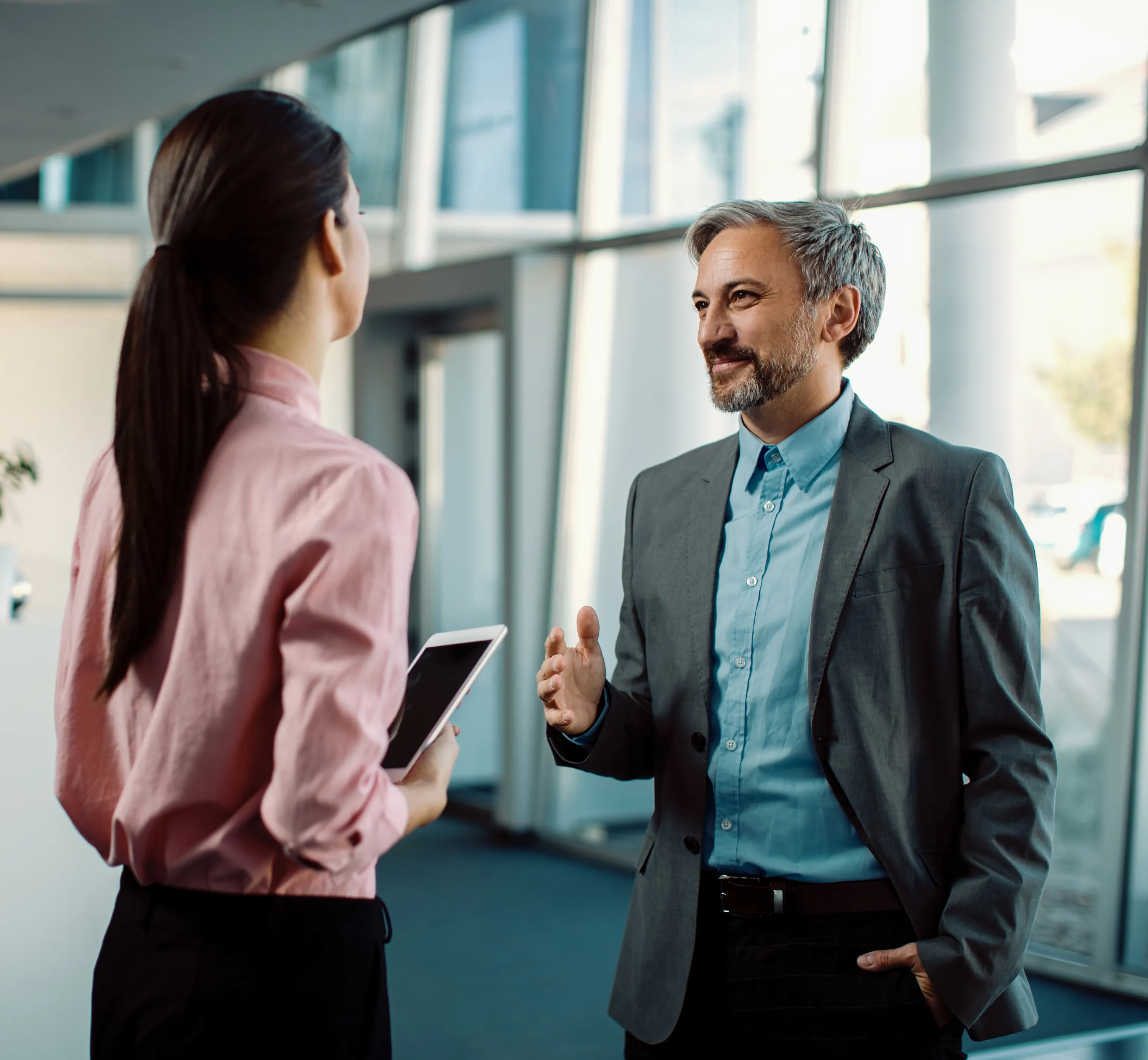 Two colleagues talking in an office corridor, one holding a tablet